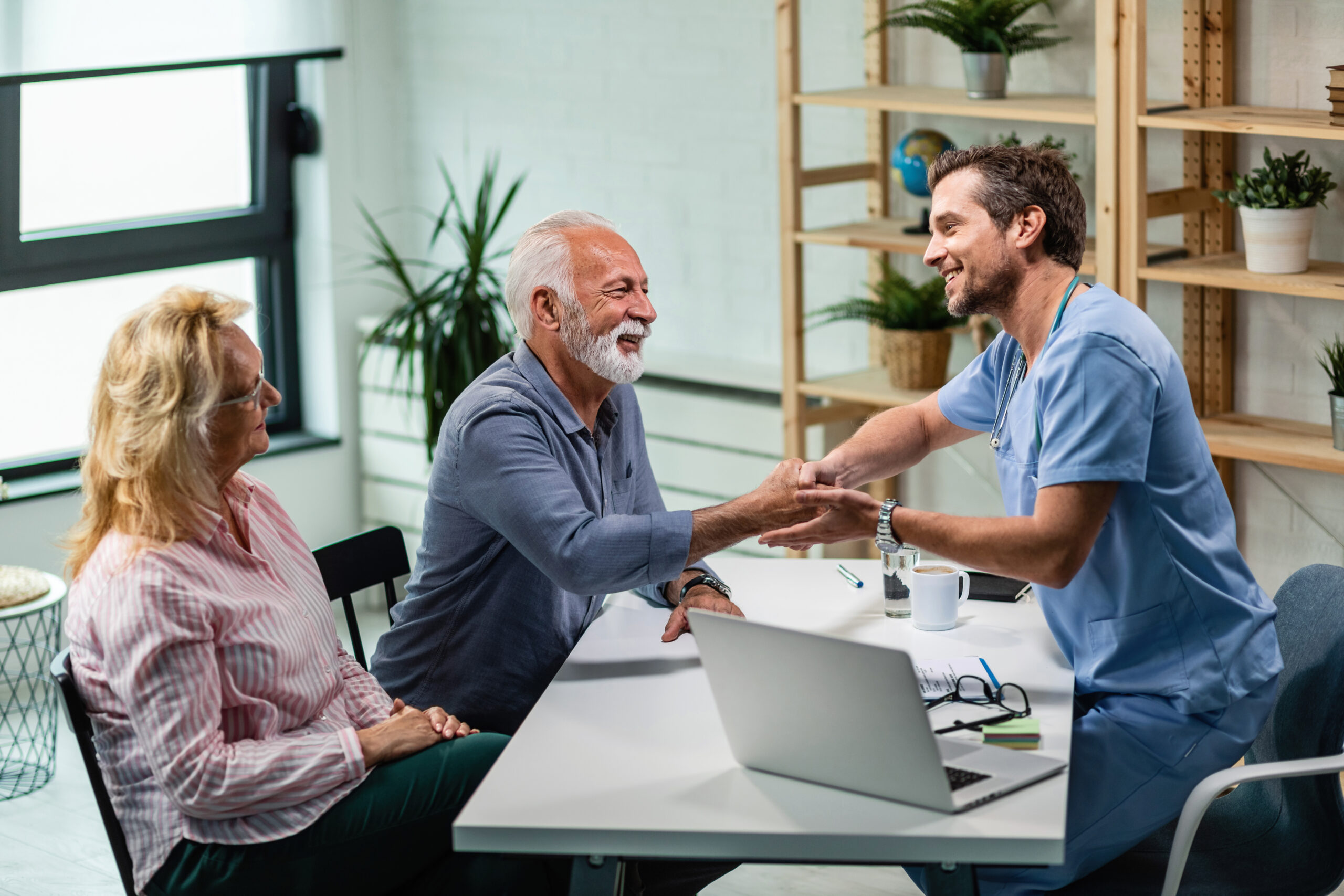 happy male doctor shaking hands with senior man who came medical appointment with his wife scaled